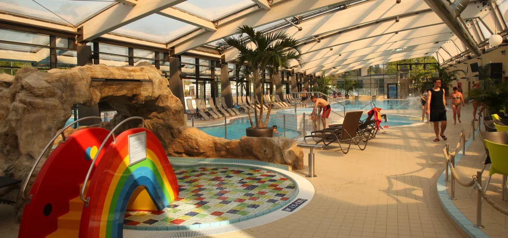 Innenpool mit einer Regenbogenrutsche und Liegestühlen im Hintergrund.