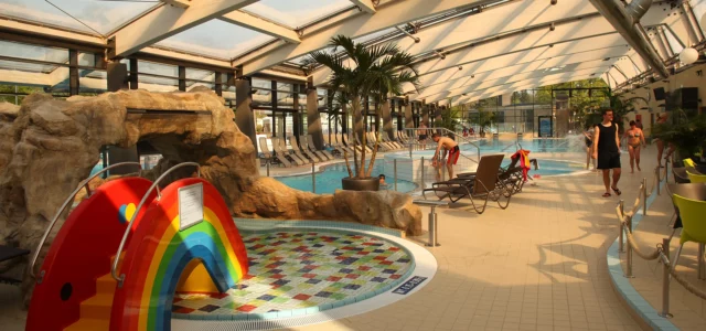 Innenpool mit einer Regenbogenrutsche und Liegestühlen im Hintergrund.