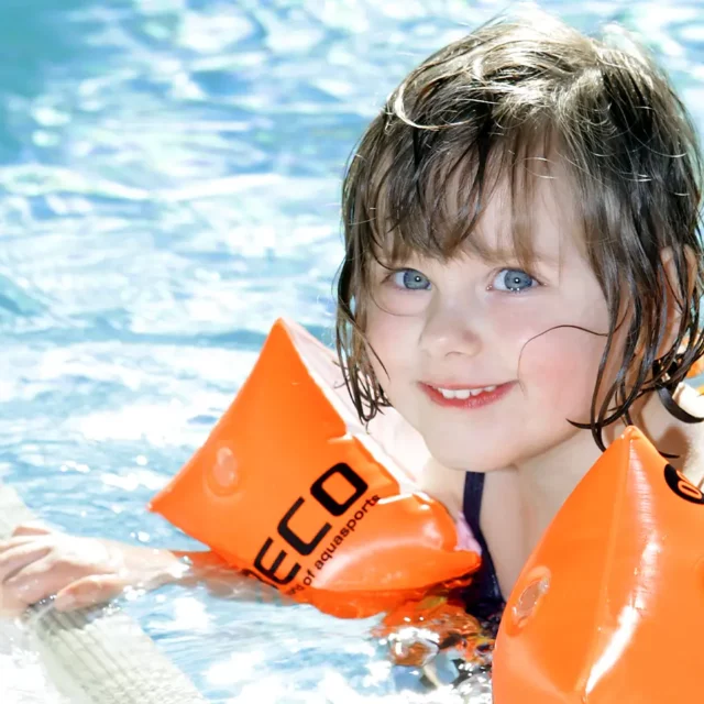 Mädchen mit Schwimmflügeln und Schwimmreifen am Beckenrand im Wasser