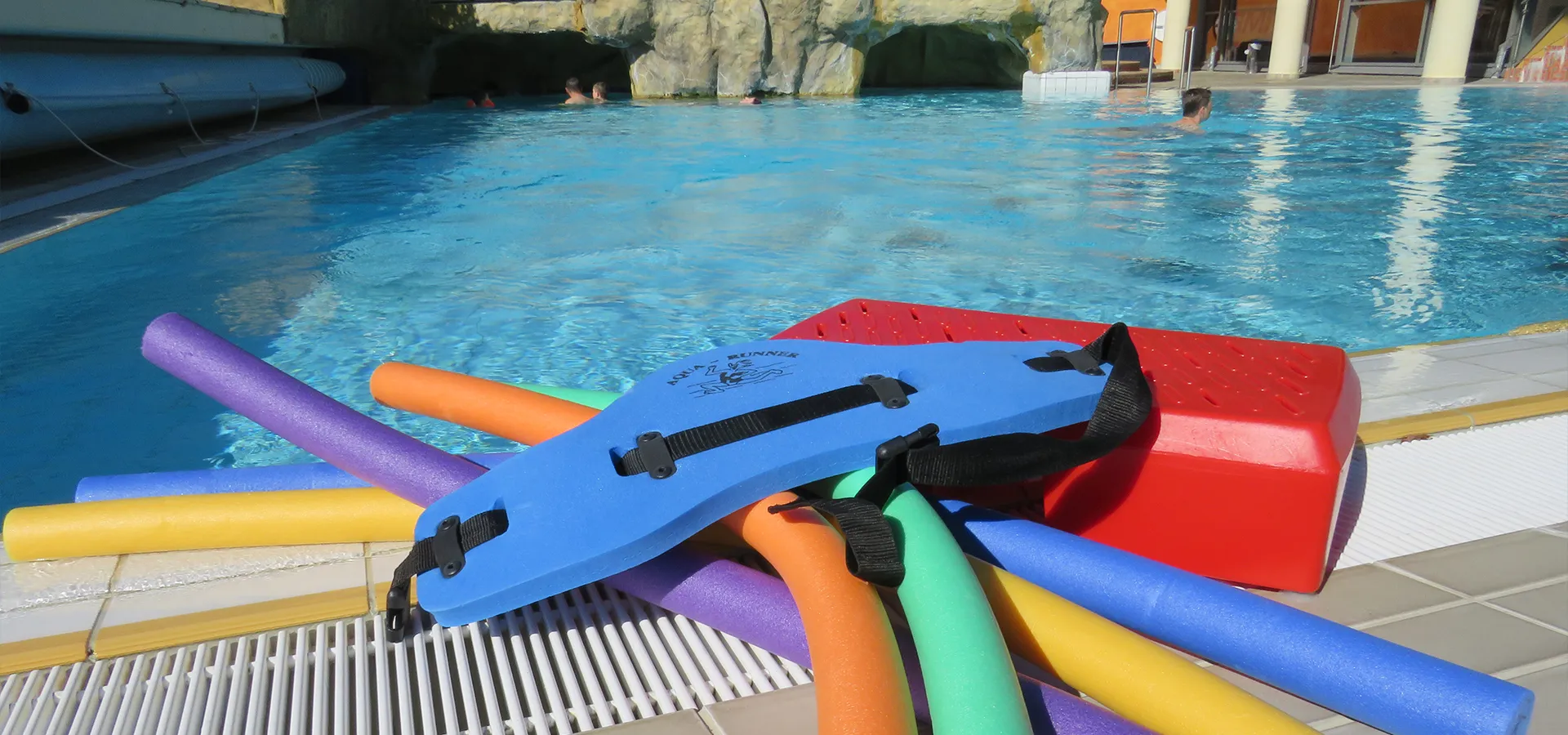 mehrer bunte Schwimmnudeln und zwei Schwimmgürtel liegen am Beckenrand