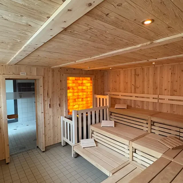 Die Sauna-Aroma-Sauna ist mit Holzwänden und -decken, gestuften Holzbänken und einer großen, beleuchteten Salzsteinwand ausgestattet.